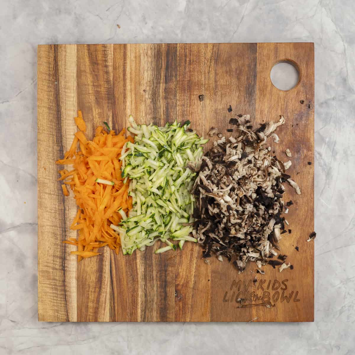 Grated carrot, zucchini and mushrooms on a wooden chopping board.