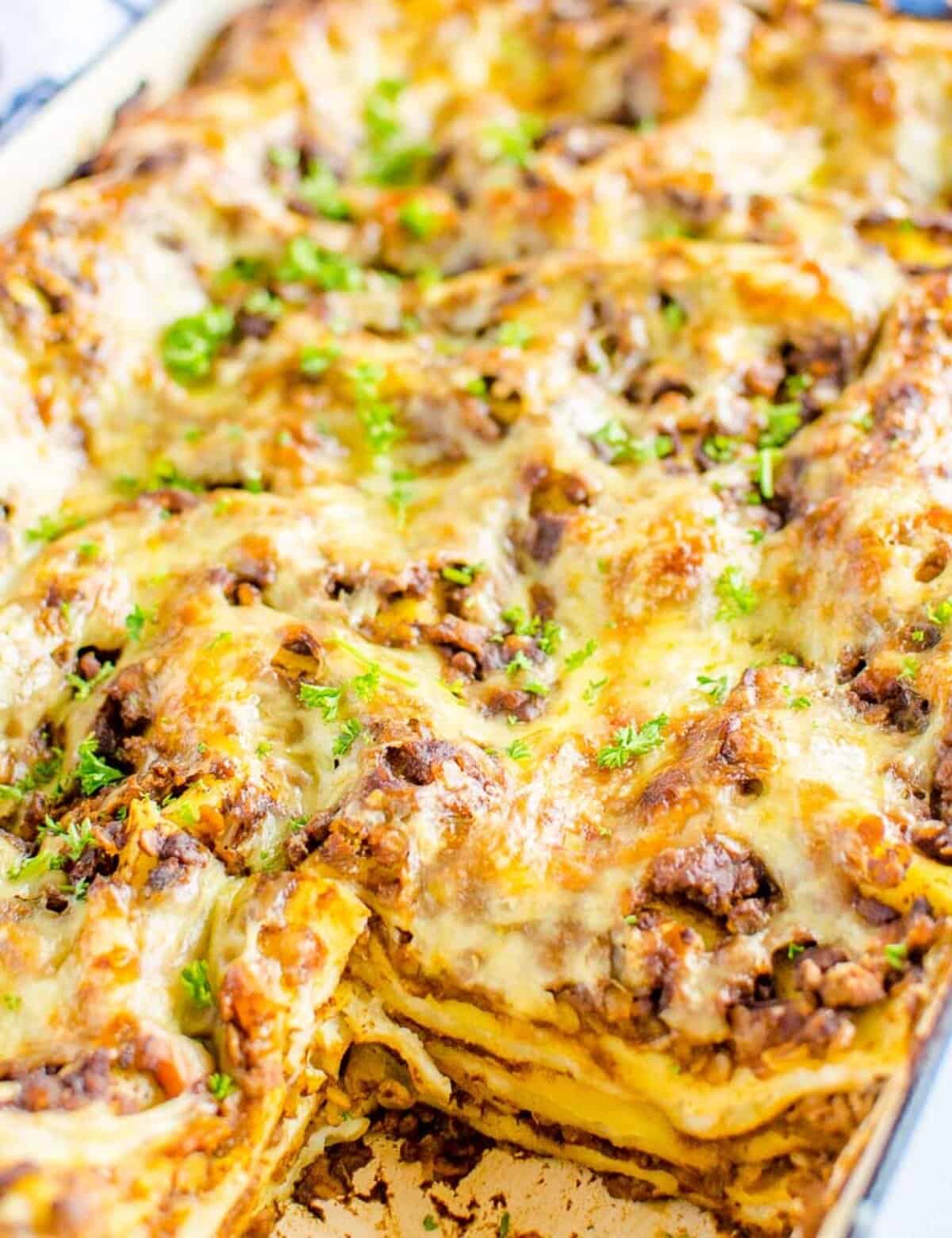 Cooked lasagna with a serving missing. Garnished with chopped parsley.