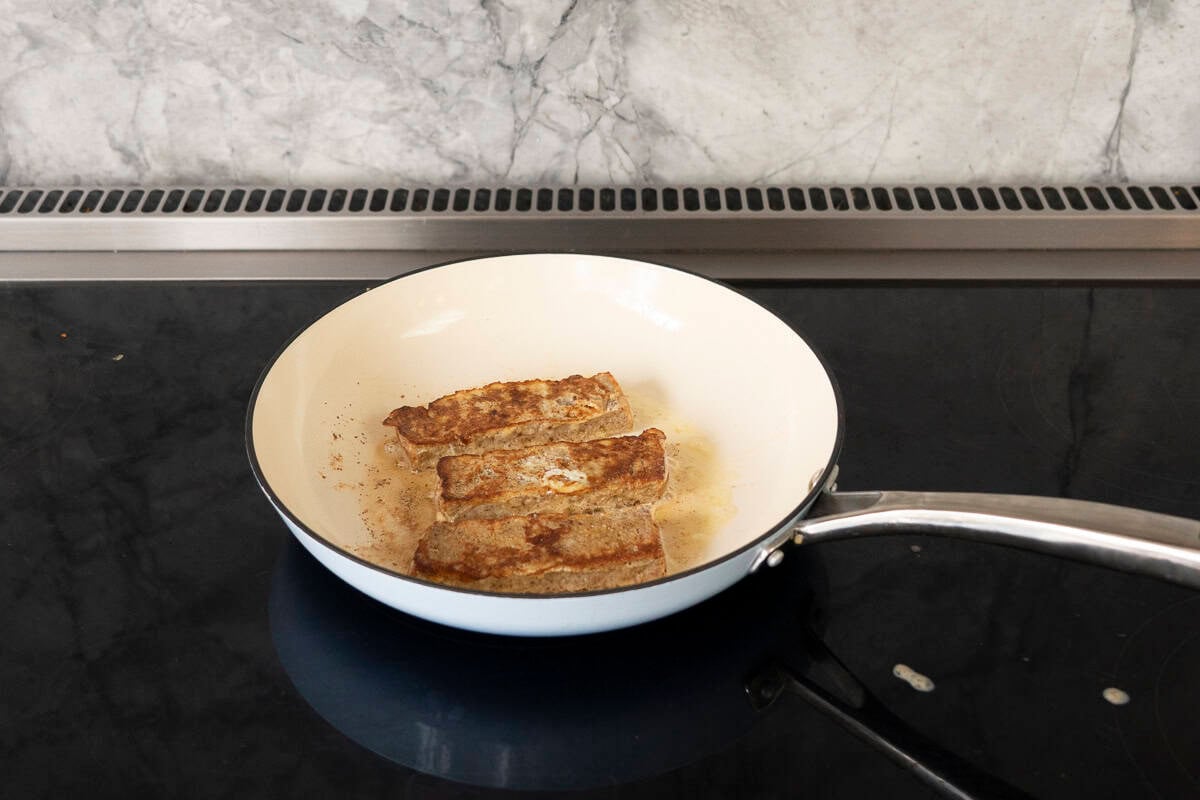 Three strips of banana French toast golden brown in a skillet with bubbling butter. 