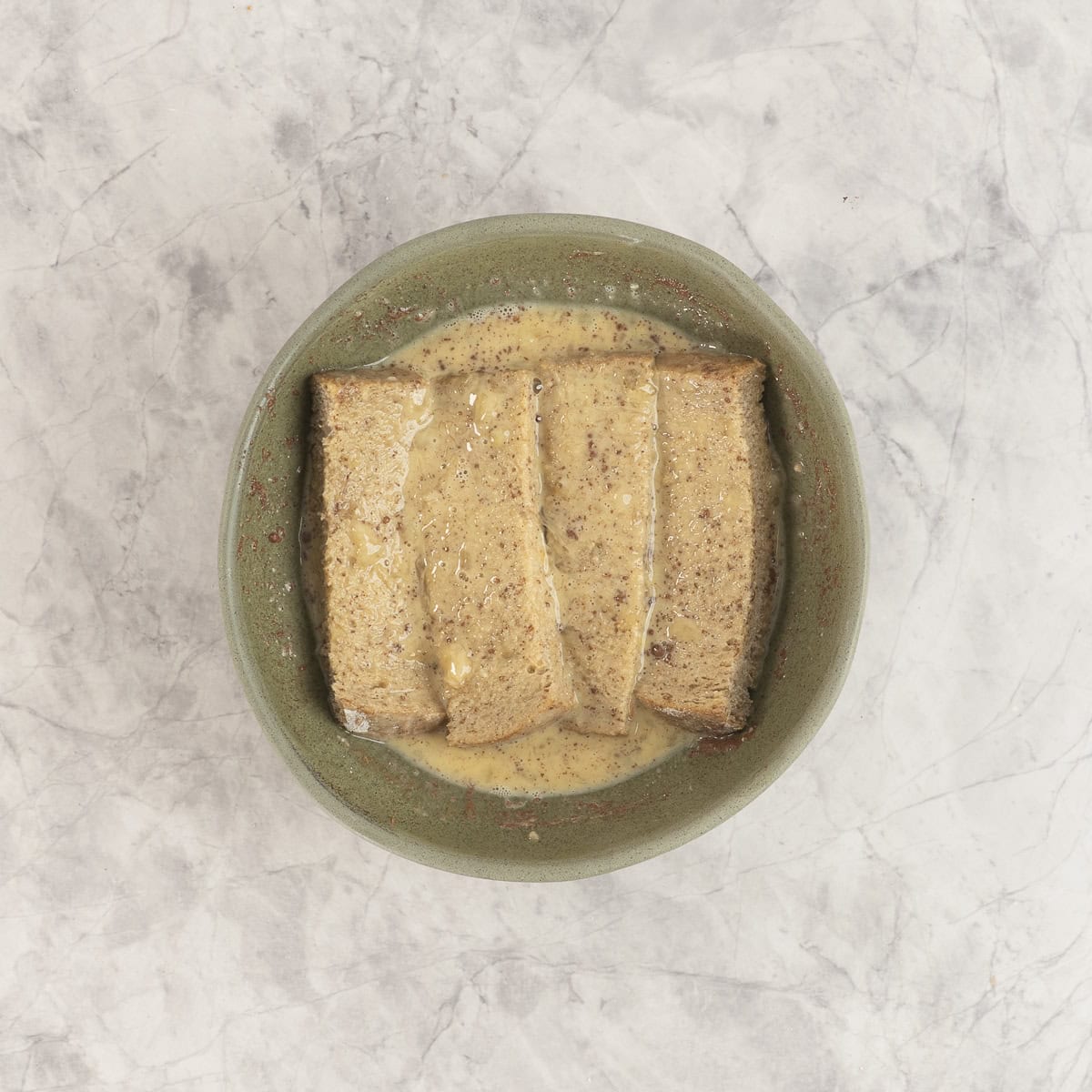 Four strips of bread soaking in French toast batter. 
