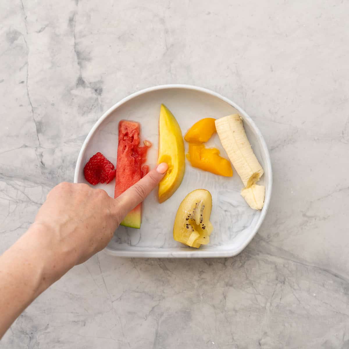 A plate of soft fruits all squashed by a finger. 