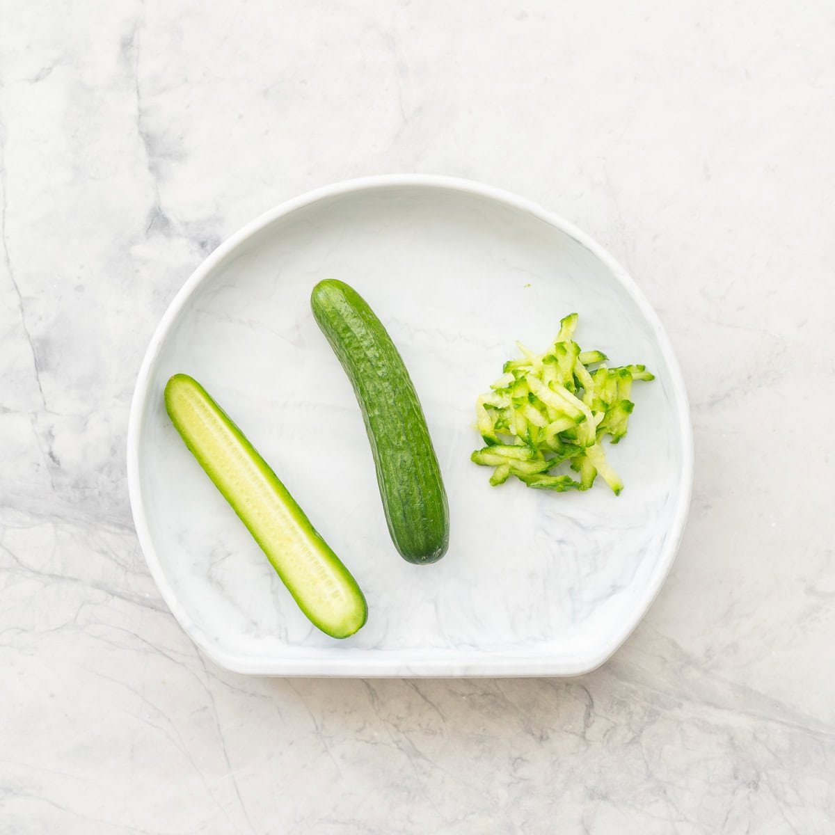 Two large sticks and a small pile of crated cucumber on a baby plate 