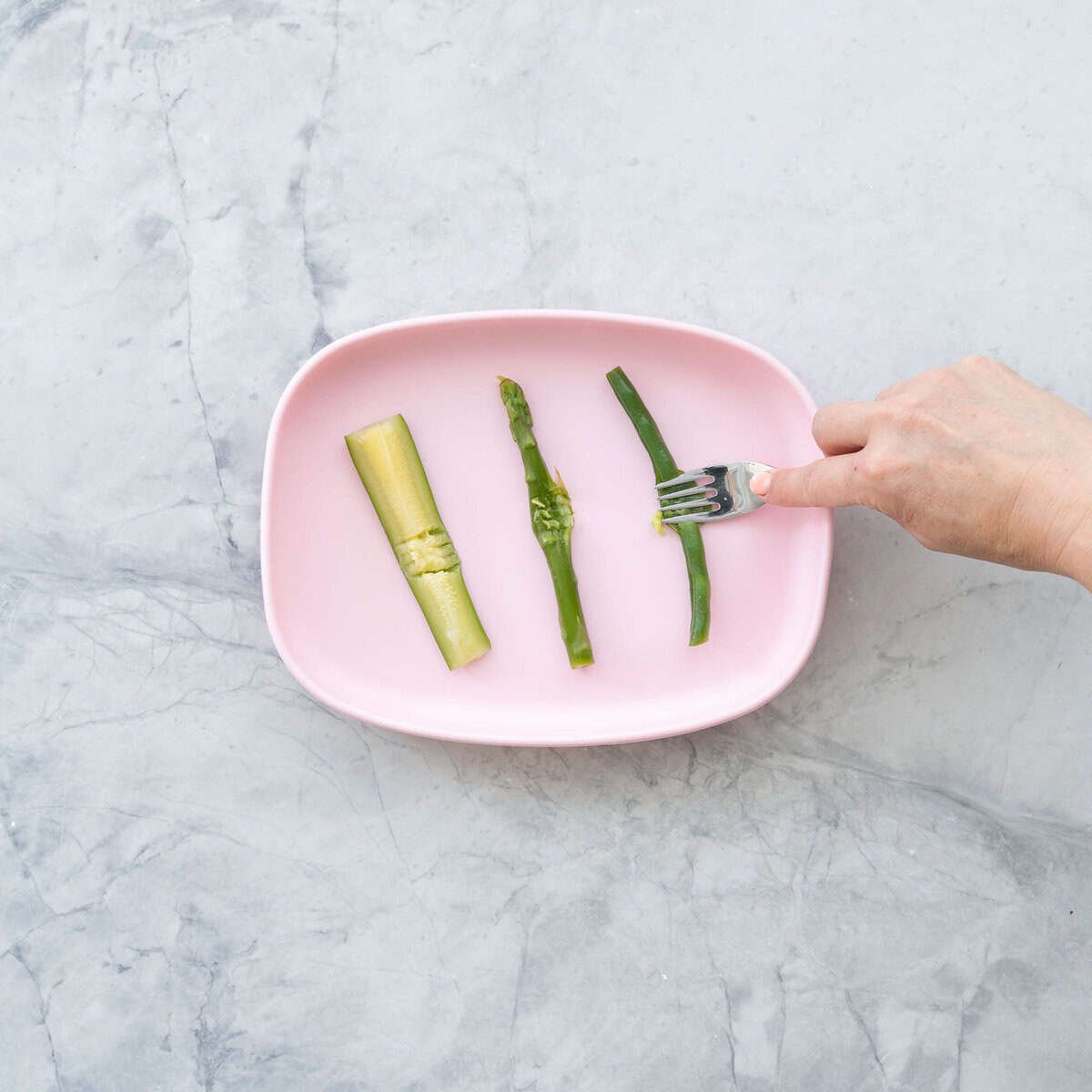 A pink baby plate with a baton of courgette squashed by a fork. 