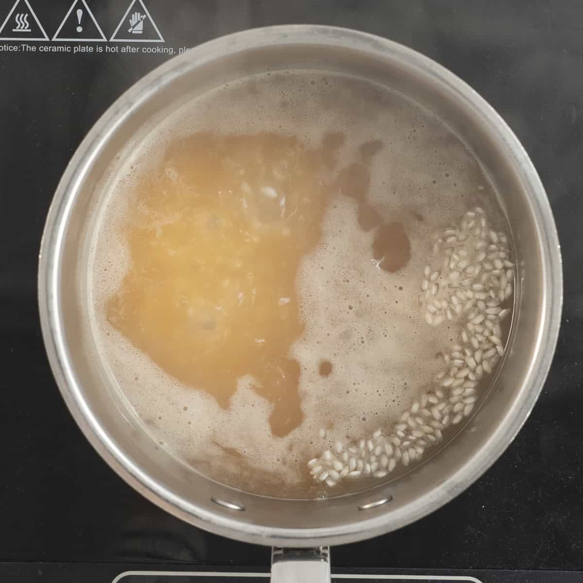 Rice and stock in a pot cooking on an electric element.