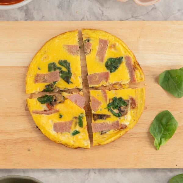 Wooden chopping board with pizza egg cut into four slices, toppings on bench top.