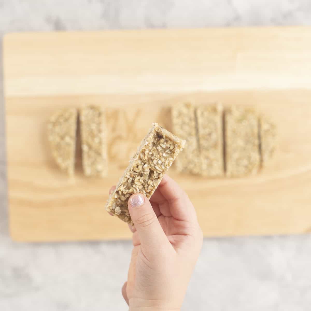Toddler hand holding a slice of porridge finger above chopping board with rest below.