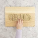 Toddler hand reaching for a porridge finger sliced on wooden chopping board.