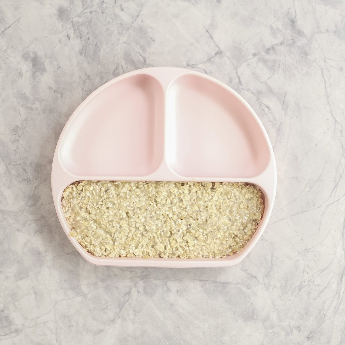 Cooked porridge in pink silicone toddler plate.