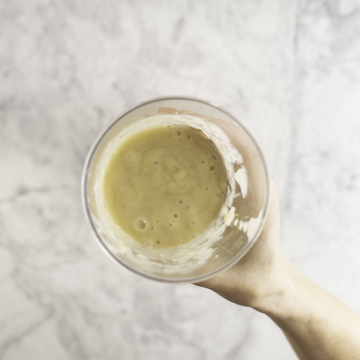 Hand holding a tall plastic cup with banana mixture inside.