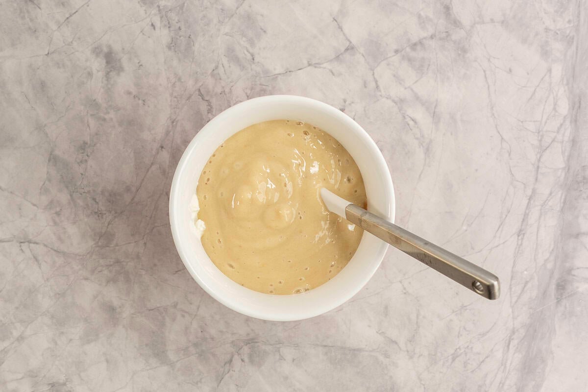 Banana mixture added into a large white bowl with dry ingredients and spatula inside.