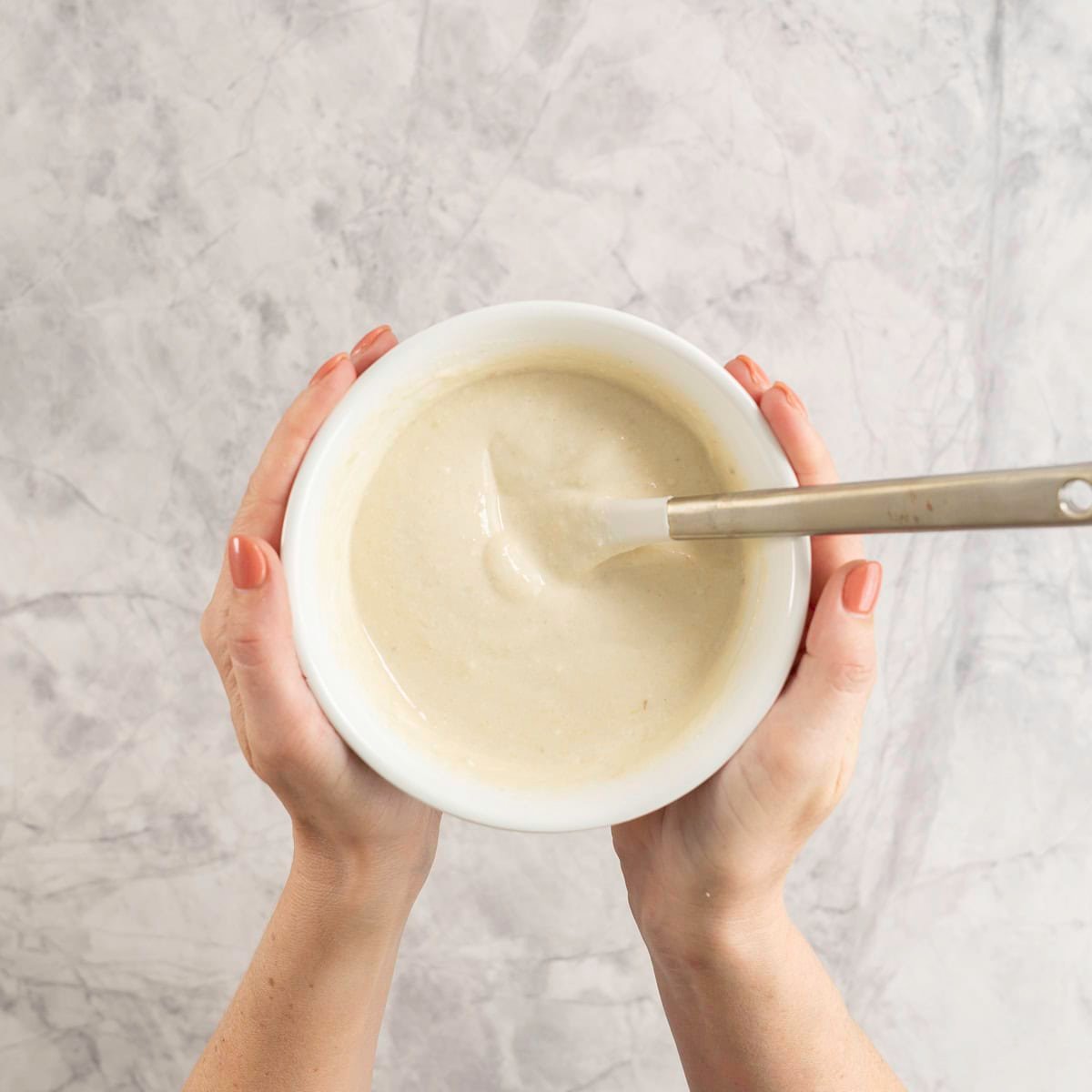 Hands holding a white bowl with creamy smooth yogurt and spatula inside.