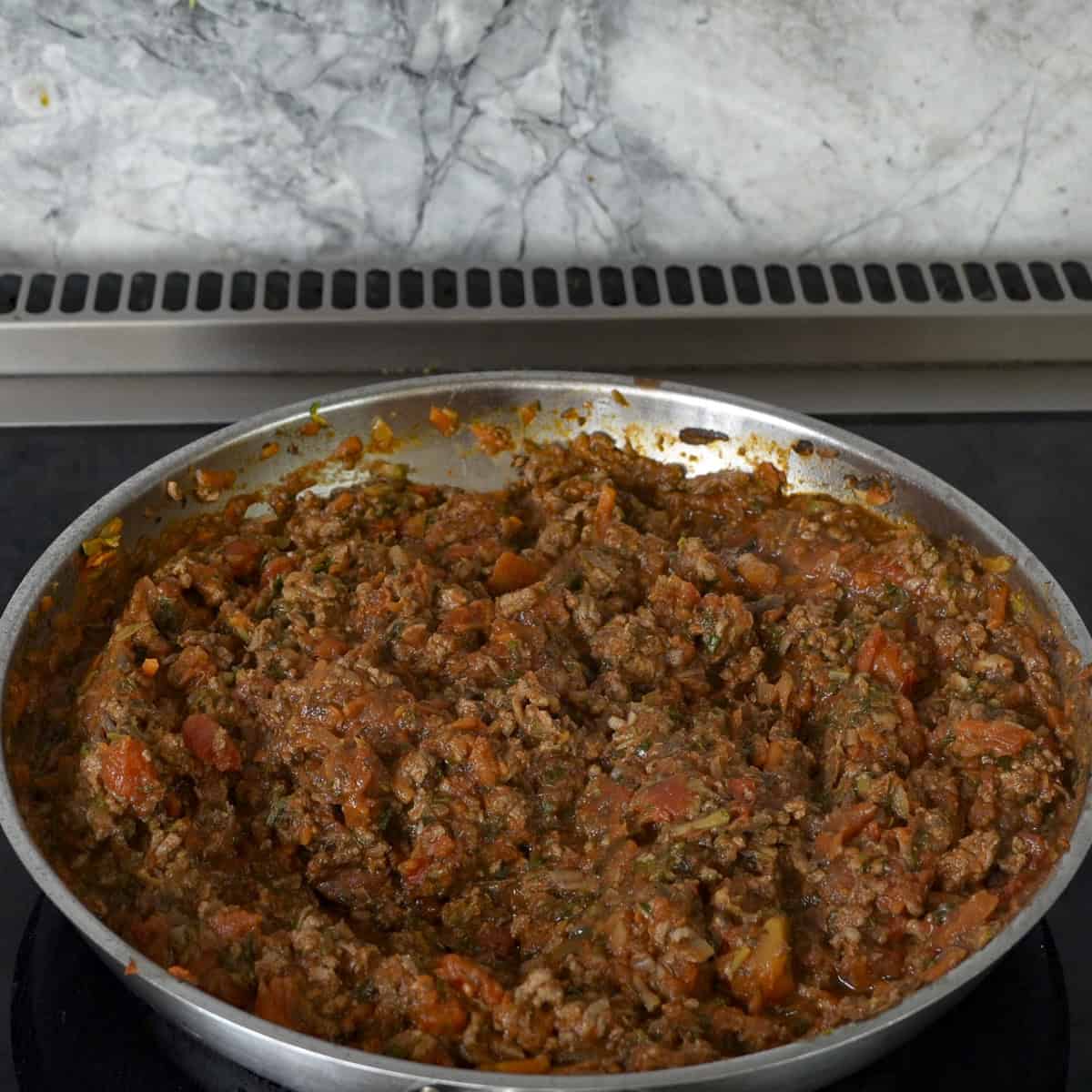Mince with tinned tomatoes and vegetables browned in a pan on stove top.