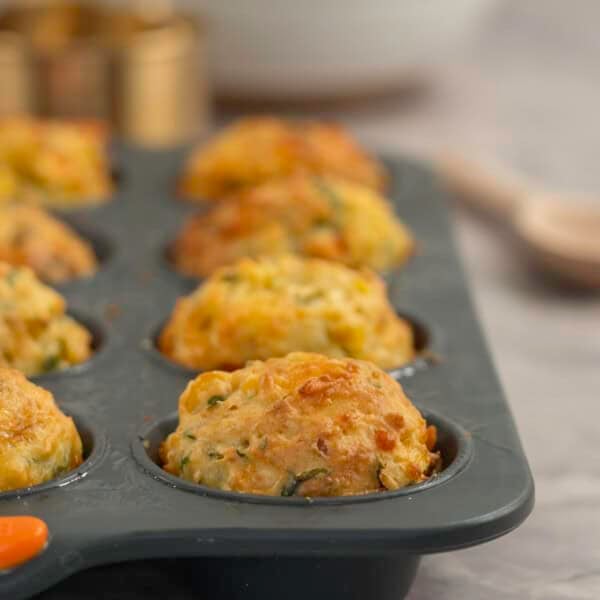Cooked muffins packed with vegetables golden in colour inside a muffin tray on bench top.