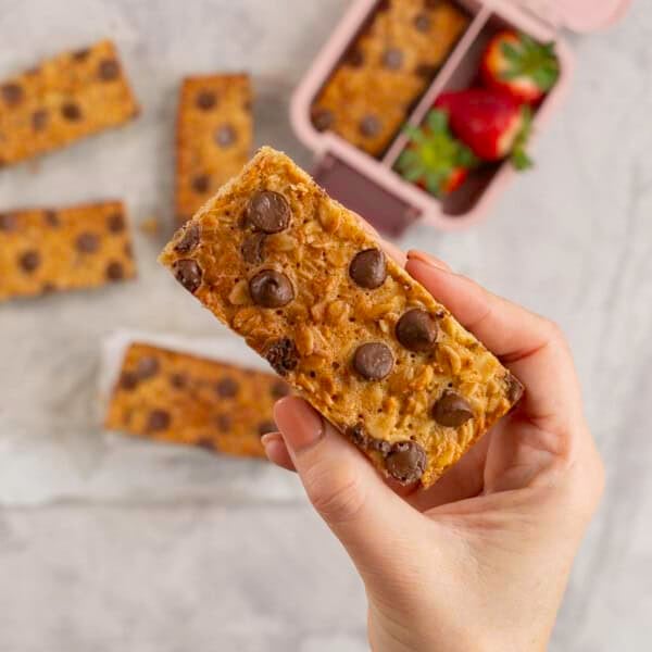 Woman's hand holding a golden granola bar with lunchbox below.