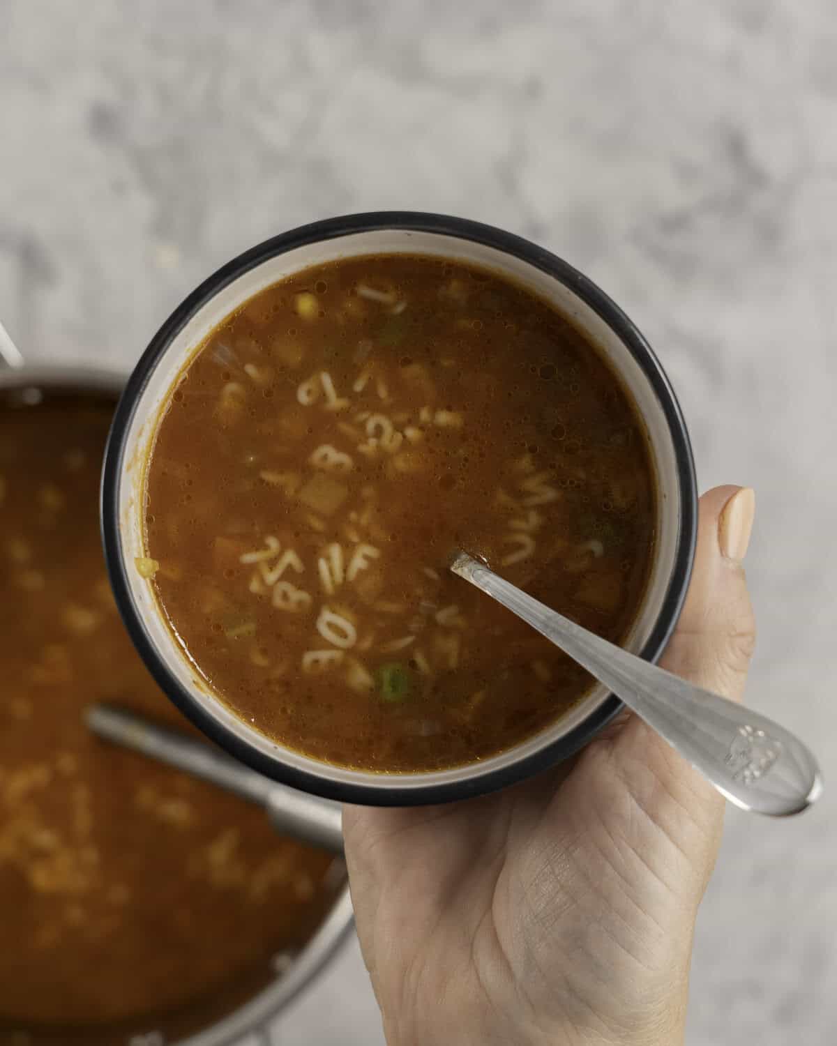 Woman's hand holding a small bowl with spoon and soup inside.