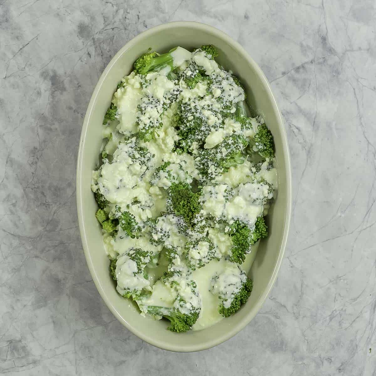 Broccoli floret's with cheese mixture poured on top inside a oval baking dish.