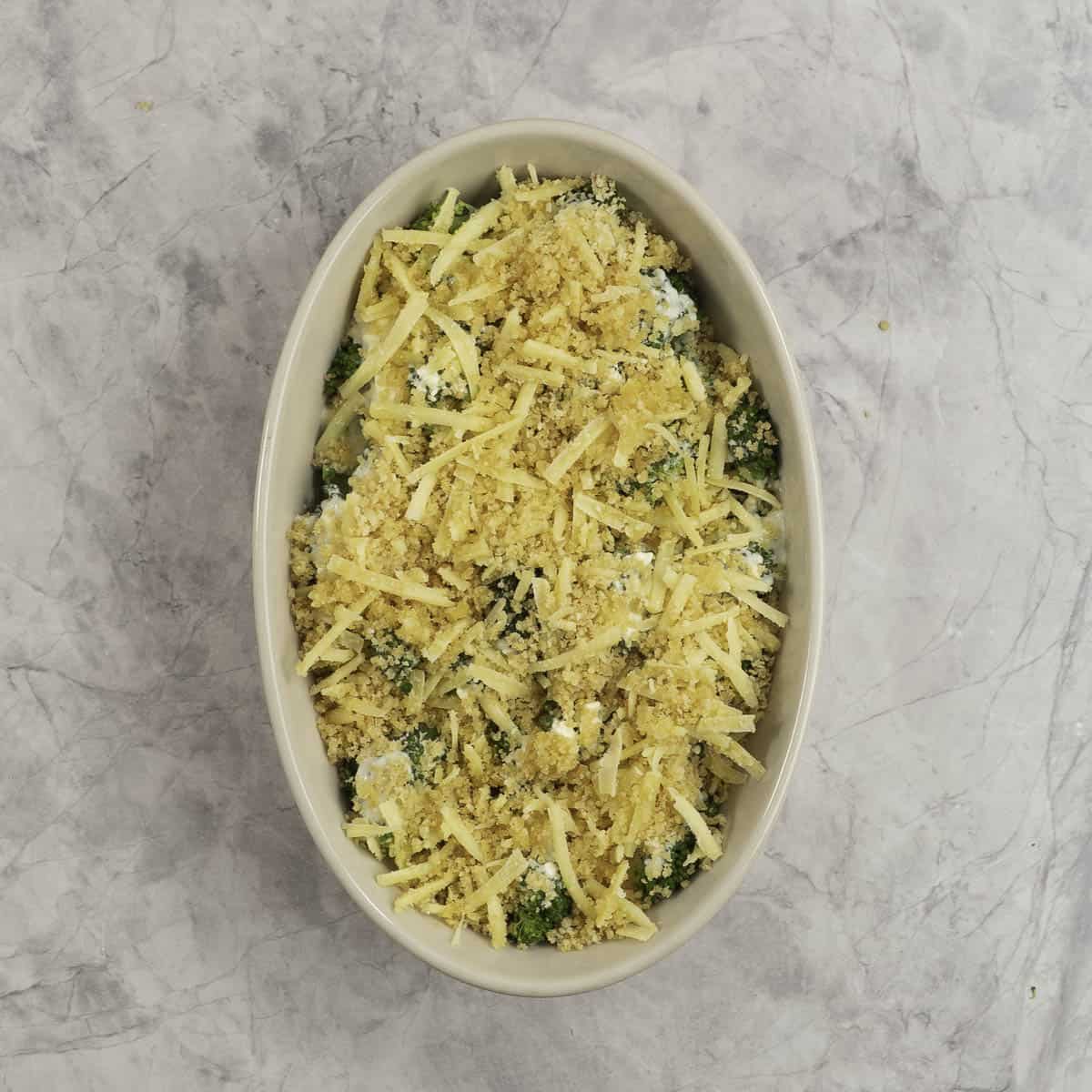 Breadcrumb cheese mixture on top of broccoli florets inside oval casserole dish.