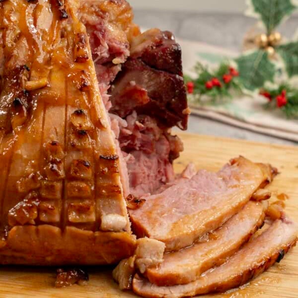 Golden glossy ham, three pieces of ham slice onto wooden chopping board.