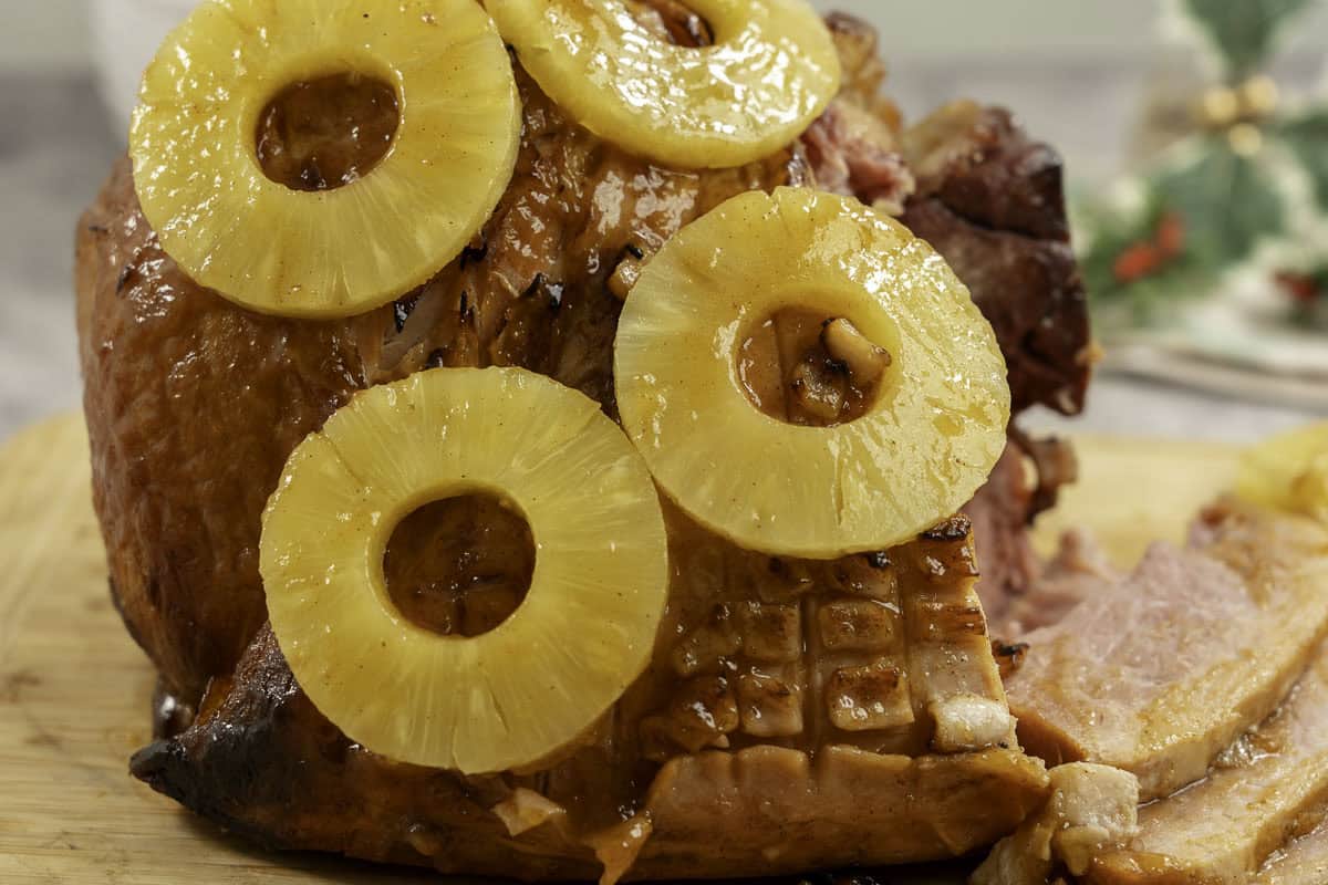 Golden glossy ham with pineapple rings placed on top, three pieces sliced from ham.