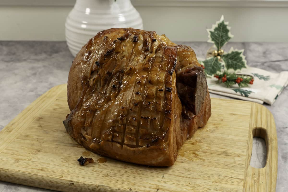 Golden glossy ham on a wooden chopping board.