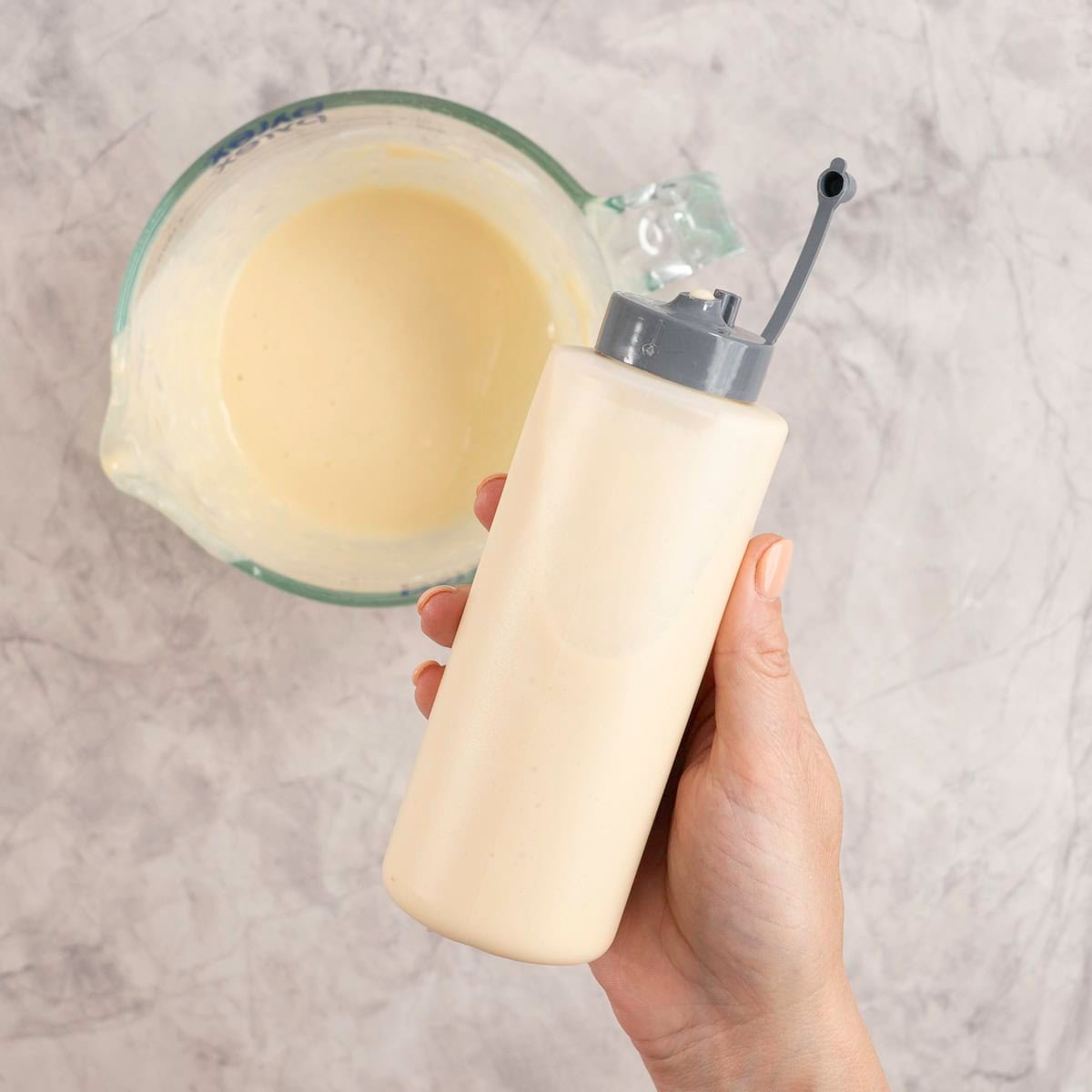 Woman holding a refillable squeezy bottle with small opening, filled with pancake mixture.