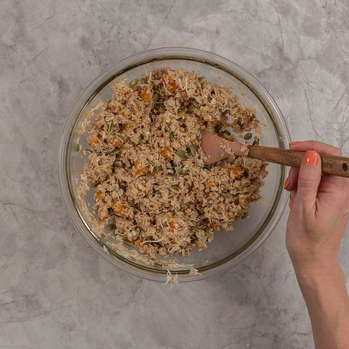 Womans hand holding a spatula mixing together ingredients for granola bars.