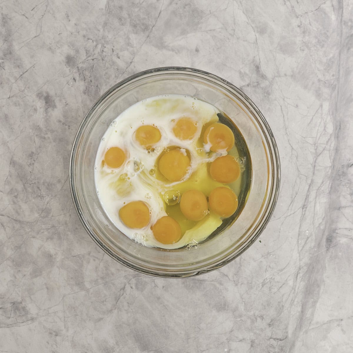 Eggs and milk in a large glass bowl on marble bench top.
