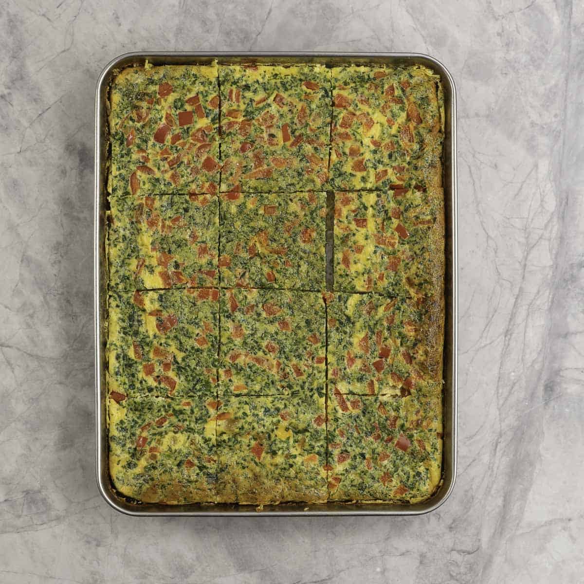 Rectangle sheet pan with eggs and vegetables cooked and cut into square pieces.