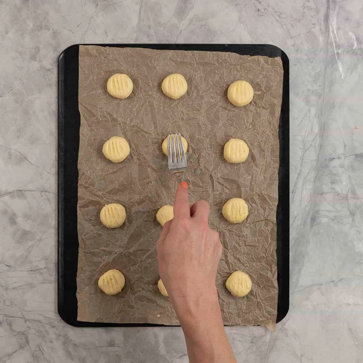 Cookie dough balls being flattened with a fork. 