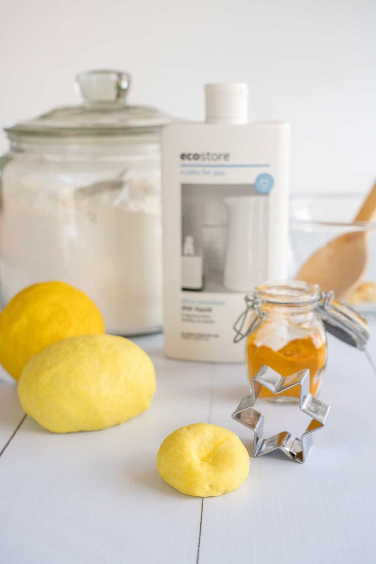 Yellow playdough on a marble bench infront of flou, turmeric and dishwashing liquid.