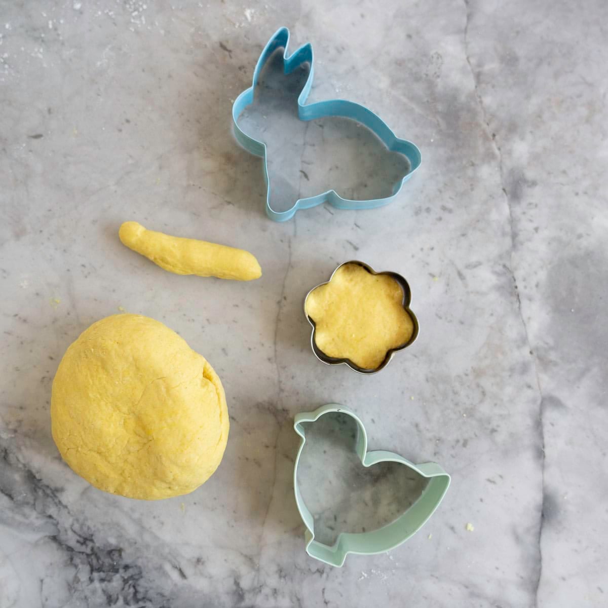 Yellow playdough and cookie cutters on a marble counter top.